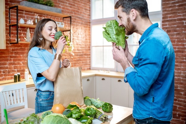 自宅のキッチンで新鮮な緑の食べ物を楽しんでいる菜食主義者の若いカップル