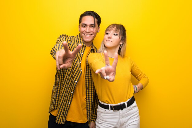 Young couple over vibrant yellow background smiling and showing victory sign