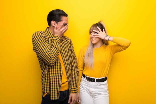 Young couple over vibrant yellow background with surprise and shocked 