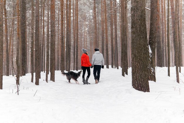 雪に覆われた冬の森で犬を散歩している若いカップル犬が遊びたい