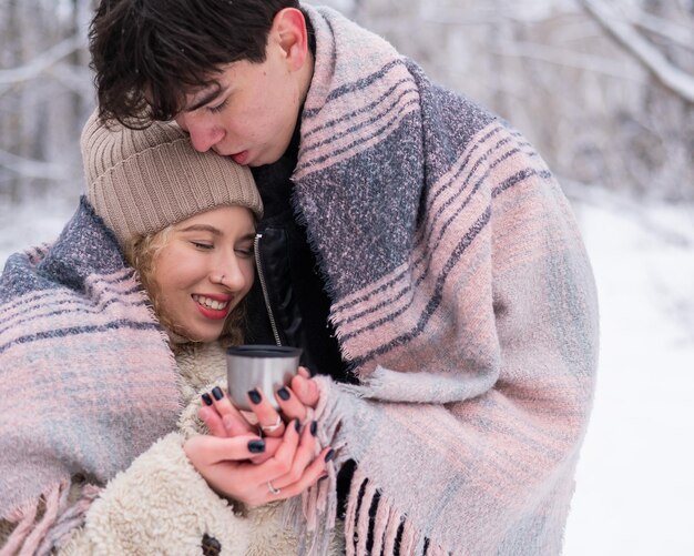 젊은 커플이 겨울에 공원을 산책합니다. 남자와 여자는 따뜻한 음료를 마시고 있습니다.