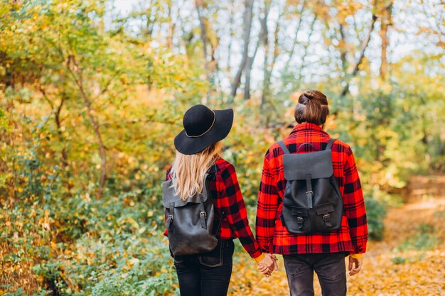 若いカップルが手を繋いでいる秋の森を歩く