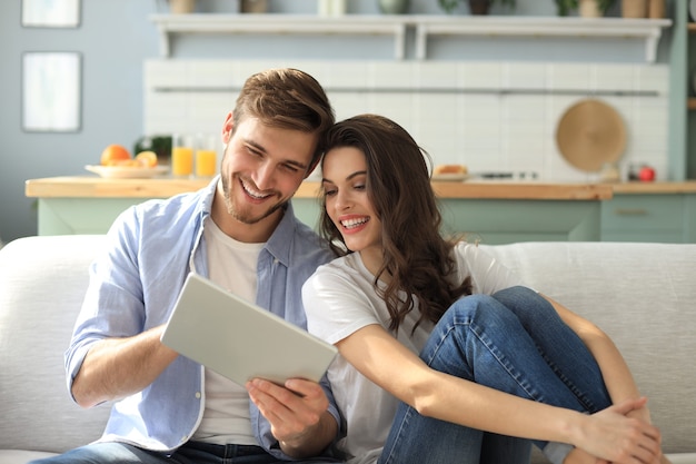 Young couple watching media content online in a tablet sitting on a sofa in the living room.