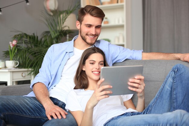 Young couple watching media content online in a tablet sitting on a sofa in the living room.