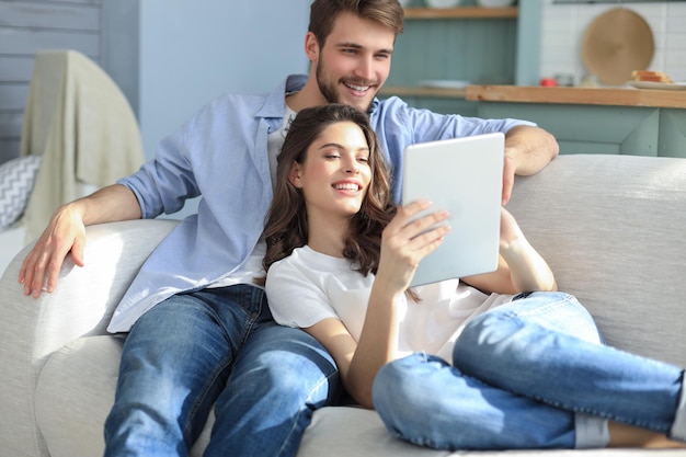 Young couple watching media content online in a tablet sitting on a sofa in the living room.