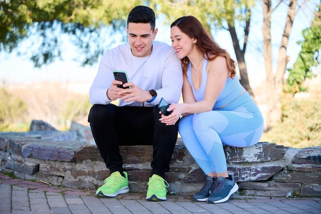 公園に座っているスマートフォンでオンラインコンテンツを見ている若いカップル