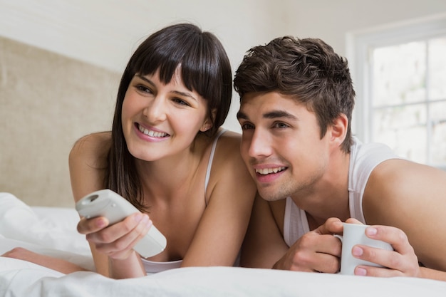 Young couple watching television together on bed in bedroom