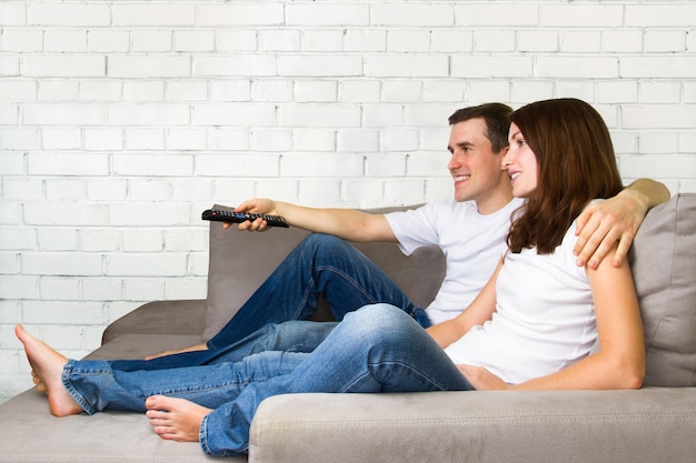 Young couple watching TV. Couple on sofa with TV remote.