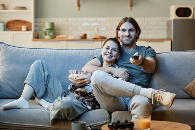 Young couple watching tv together sitting on sofa and holding remote control