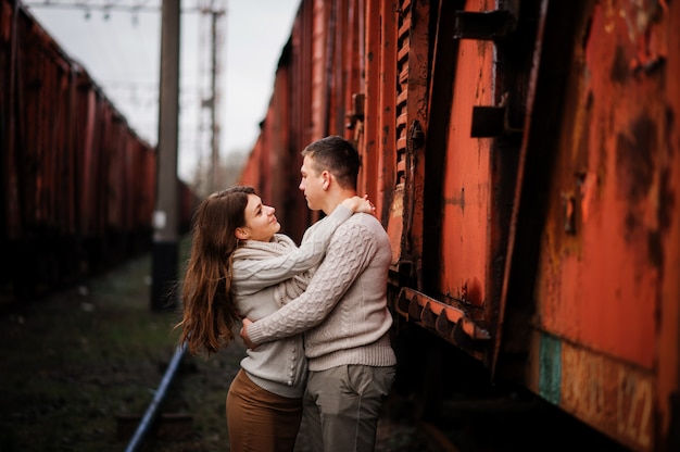 Young couple wearing on tied warm sweaters hugging in love at railway stations 