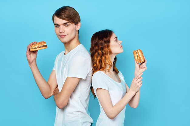 Young couple in white tshirts with hamburgers in their hands fast food snack