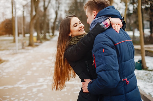 A young couple in winter jackets and scarves walk in a snowy park