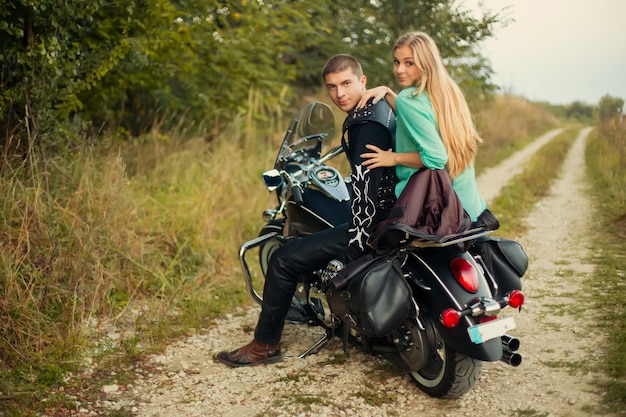 Young couple with beautiful motorbike on road.