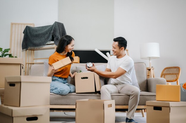 大きな箱を持った若いカップルが新しい家に引っ越しますカップルのための新しいアパート若いアジア人男性と女性が新しい家のためにソファに箱を持ち上げるのを手伝っています 引っ越しハウスXA
