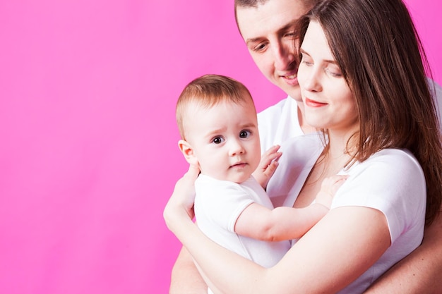 The young couple with a cute little baby huging and posing on the camera