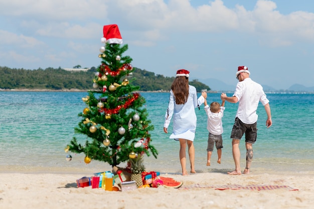 Coppia giovane con il figlio carino sulla spiaggia. concetto di celebrazione del natale.