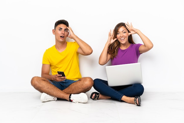 Young couple with a laptop sitting on the floor on white with surprise expression