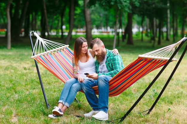 Young couple with mobile phone sitting on hammock