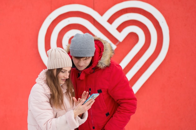 Young couple with phone in the city near big heart on the wall