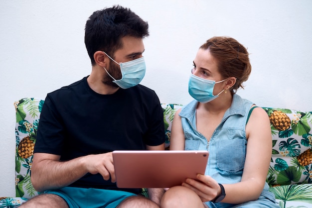 Young couple with surgical masks using a tablet