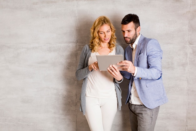 Young couple with tablet standing by the wall