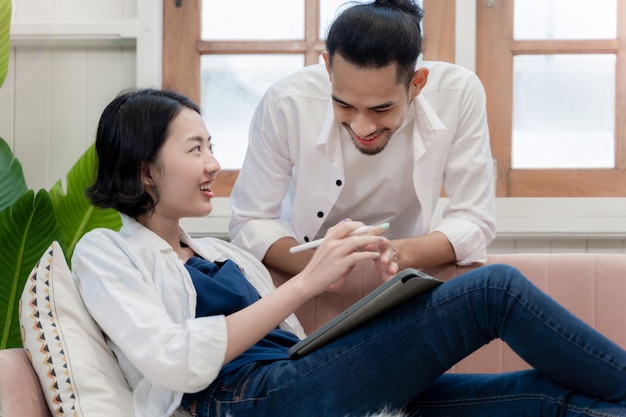 Young couple working together at home woman sit on sofa with tablet and man watching her working