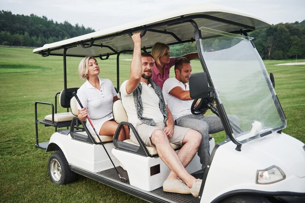 Young couples getting ready to play. A group of smiling friends came to the hole on a golf cart