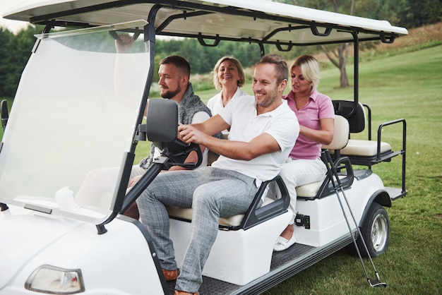 Giovani coppie si preparano a giocare. un gruppo di amici sorridenti venne alla buca su un carrello da golf