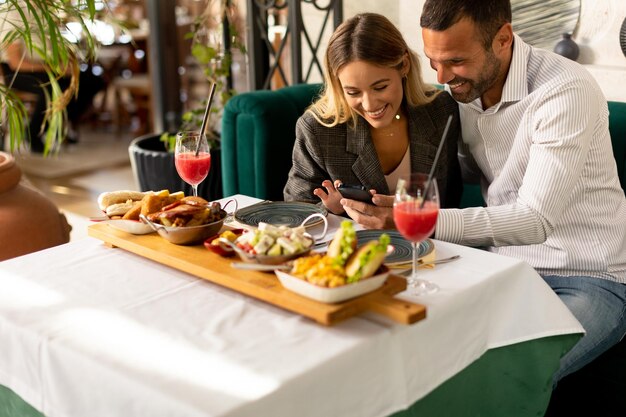 レストランで昼食をとり新鮮なジュースを飲みながら携帯電話を使っている若いカップル