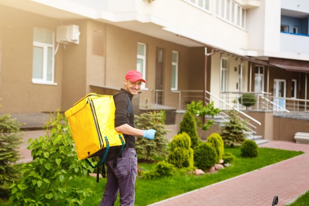 Young courier with thermo bag near the house. Food delivery service