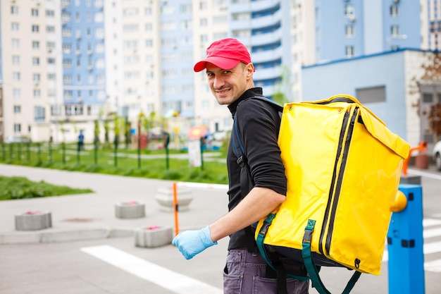 Young courier with thermo bag near the house. Food delivery service