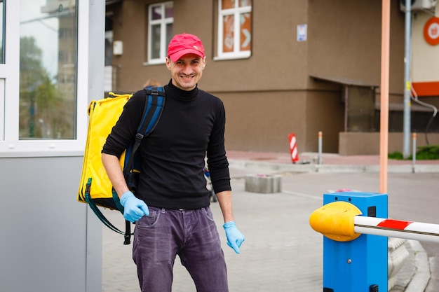 Young courier with thermo bag near the house. Food delivery service