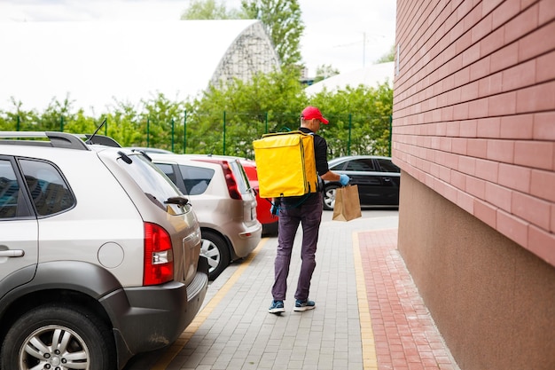 Young courier with thermo bag near the house. Food delivery service