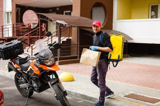 Young courier with thermo bag near the house. Food delivery service