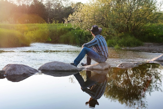 Young cowboy admires the sunset in the spring evening on the river