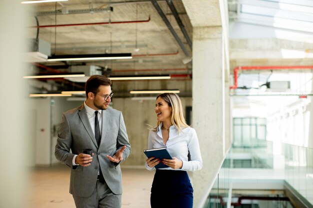 Young coworkers walking and talking along corridor in modern office