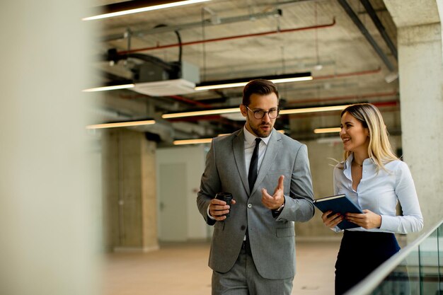 Young coworkers walking and talking along corridor in modern office