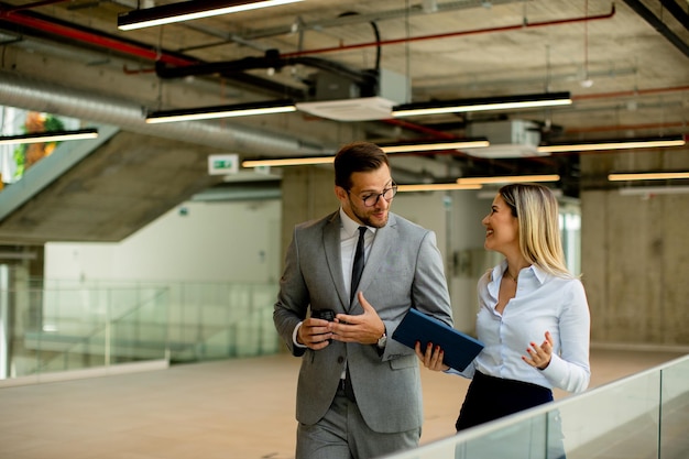 Young coworkers walking and talking along corridor in modern office