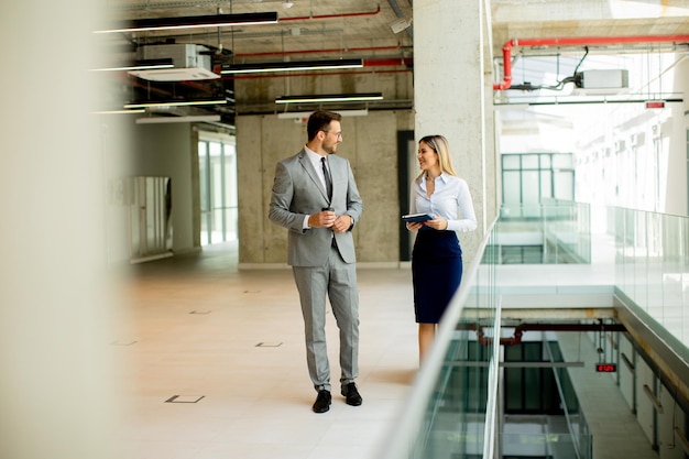 Young coworkers walking and talking along corridor in modern office