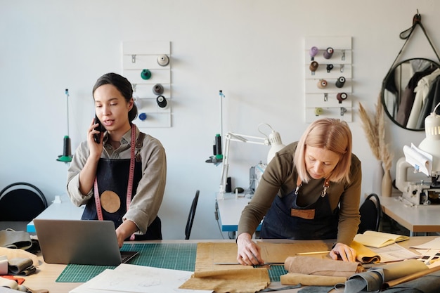 Photo young craftswoman talking to client on smartphone and using laptop