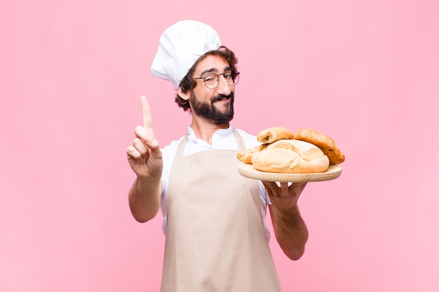 Young crazy baker man holding bread on pink wall