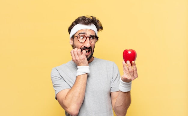 Молодой сумасшедший бородатый спортсмен напуган выражением лица и держит яблоко и держит яблоко