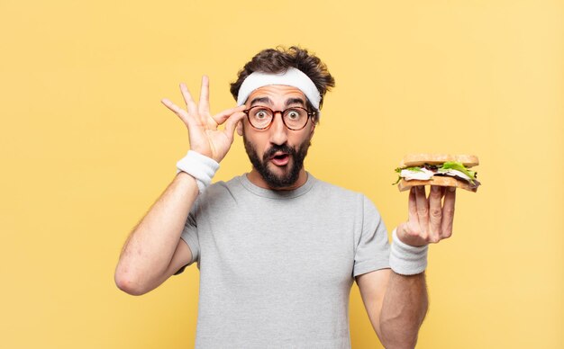 Young crazy bearded athlete surprised expression and holding a sandwich