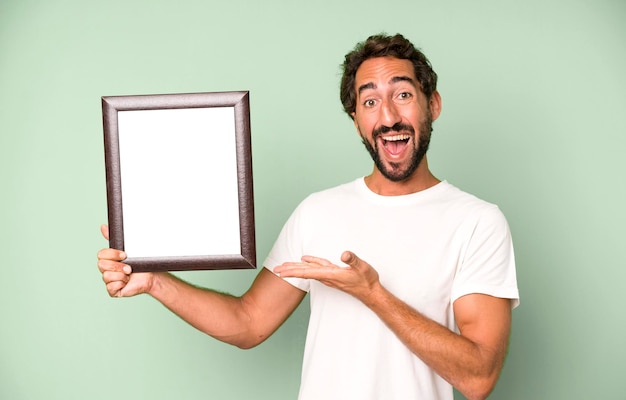 Young crazy bearded and expressive man holding a white empty frame