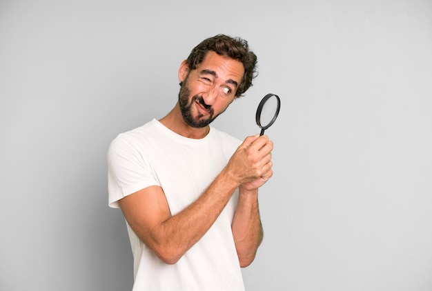 Young crazy bearded and expressive man with a magnifying glass\
search or find concept