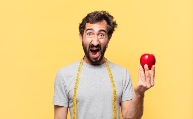 Young crazy bearded man dieting angry expression and holding an apple