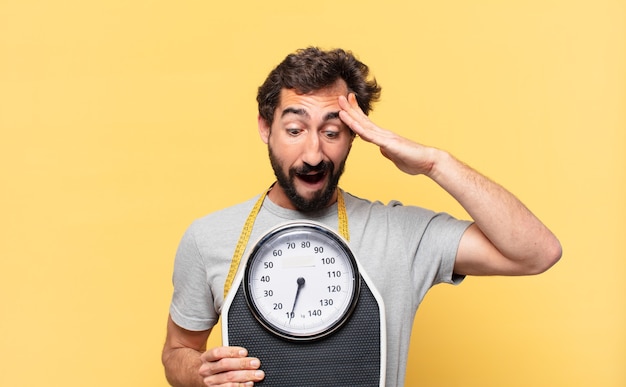 Young crazy bearded man dieting scared expression and holding a sweight scale