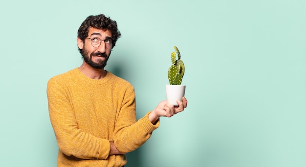 Foto giovane uomo barbuto pazzo che tiene una pianta della casa del cactus