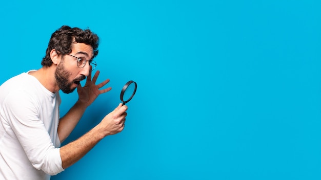 Photo young crazy bearded man looking and trying to find with a magnifying glass