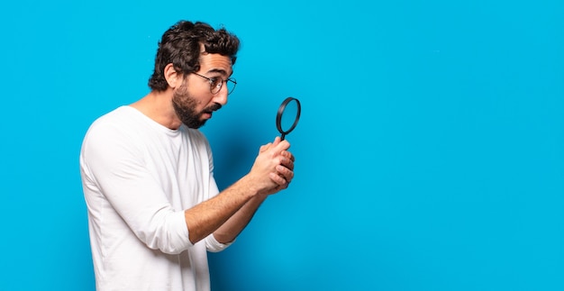 Foto giovane uomo barbuto pazzo cercando e cercando di trovare con una lente d'ingrandimento